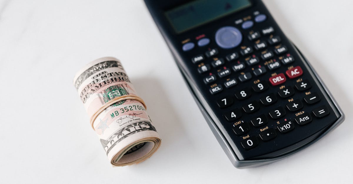 From above of modern electronic calculator with small display and buttons of different colors near roll of dollar bills on marble surface