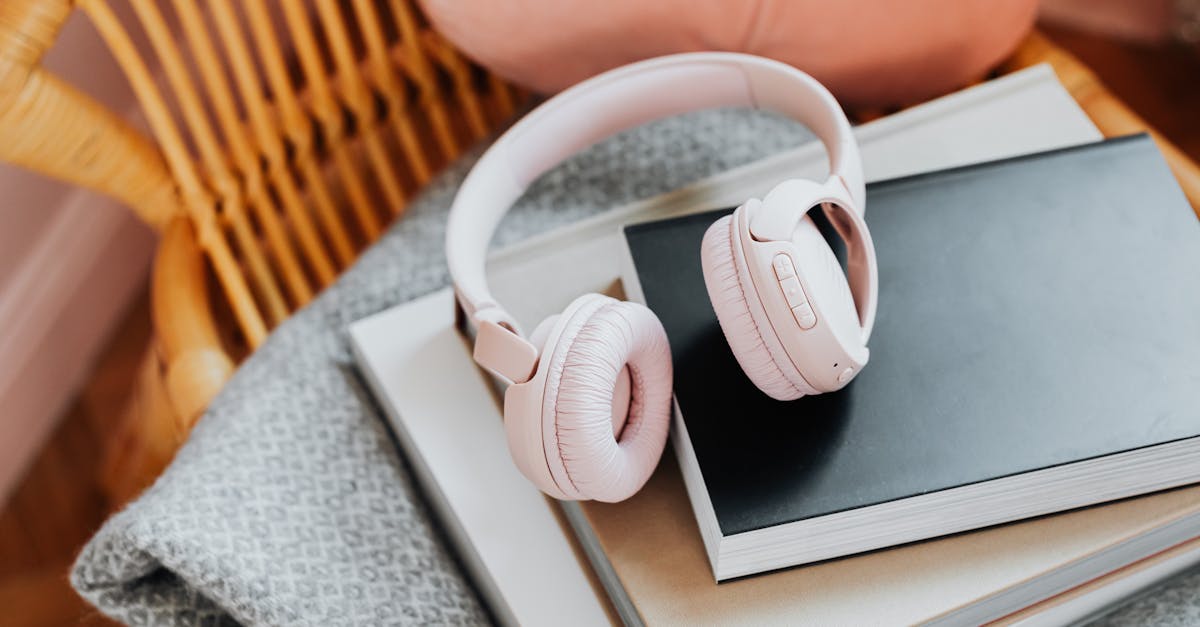 Pink wireless headphones resting on a stack of books on a rattan chair, enhancing a cozy vibe.